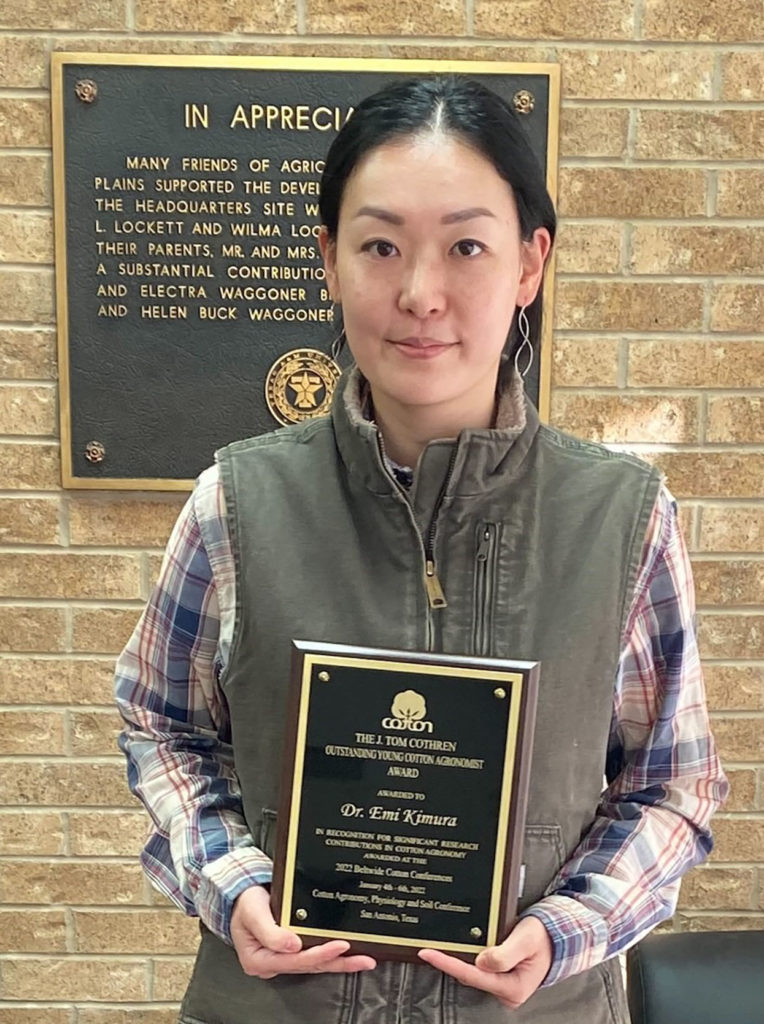 A woman, Emi Kimura, stands holding a plaque she received for the Dr. J. Tom Cothren Award for Outstanding Research in Cotton.