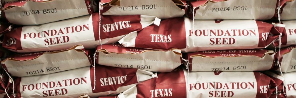 bags of seed piled on top of one another with Foundation Seed Service Texas words on them.
