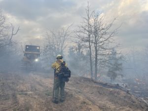 Dozier digging fire line with fireman standing watch