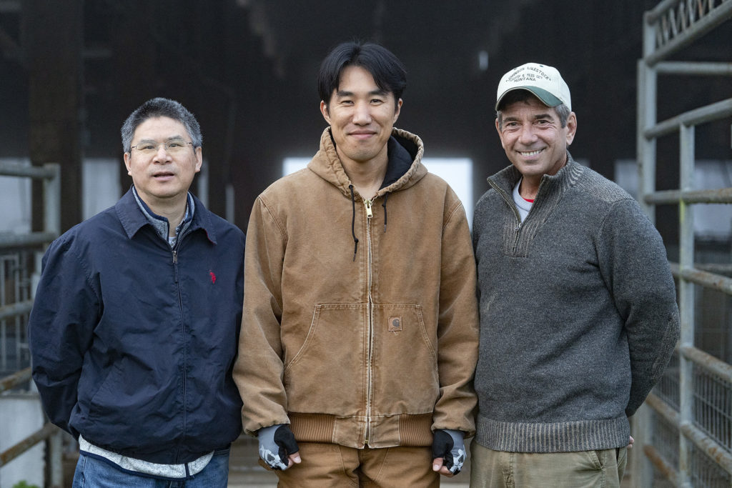 Three men stand in front of outdoor livestock pens
