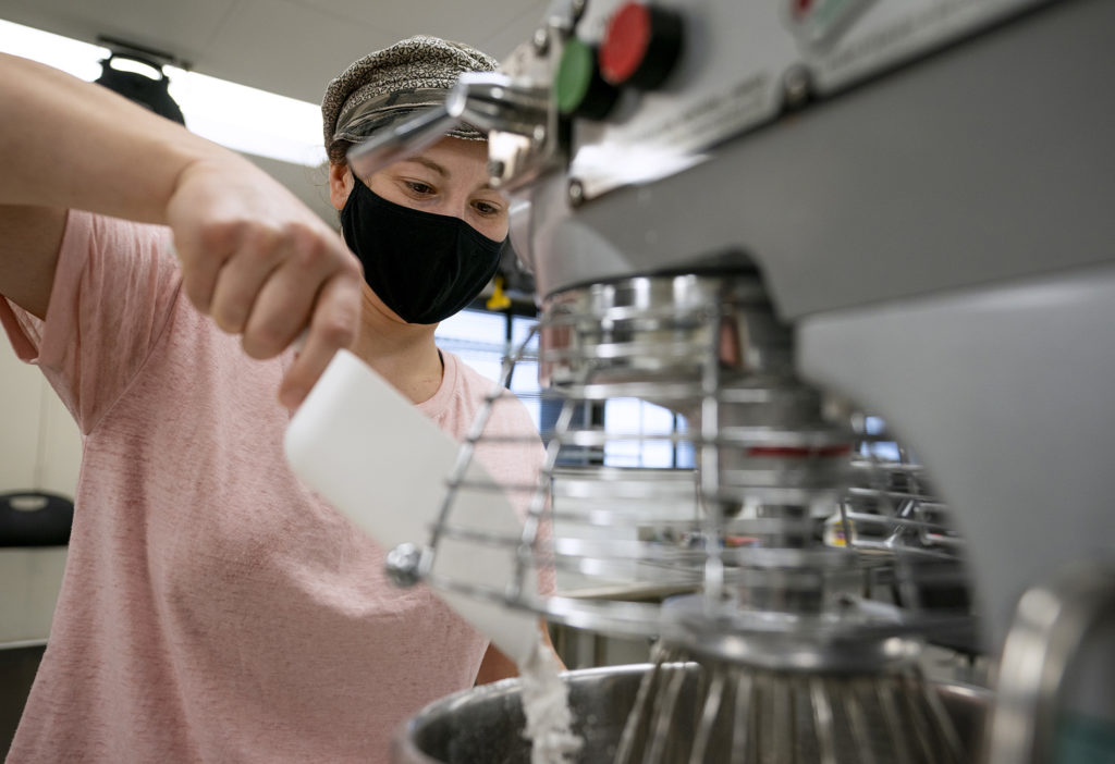 A masked female student pours flour into a mixer