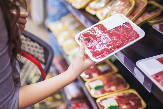 an arm holds up a package of meat in a supermarket setting.