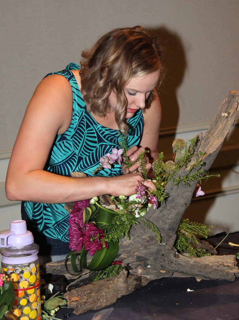 Female creating a floral arrangement in a hollowed out tree branch.