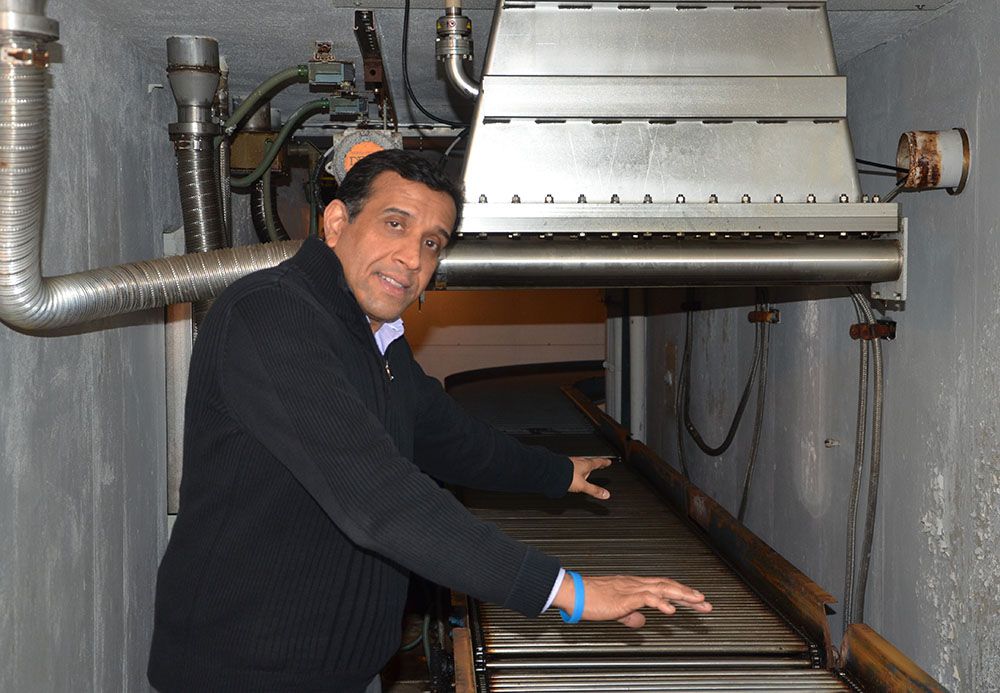 A man, Suresh Pillai, stands inside a metal eBeam chamber with a roller belt used for food safety 