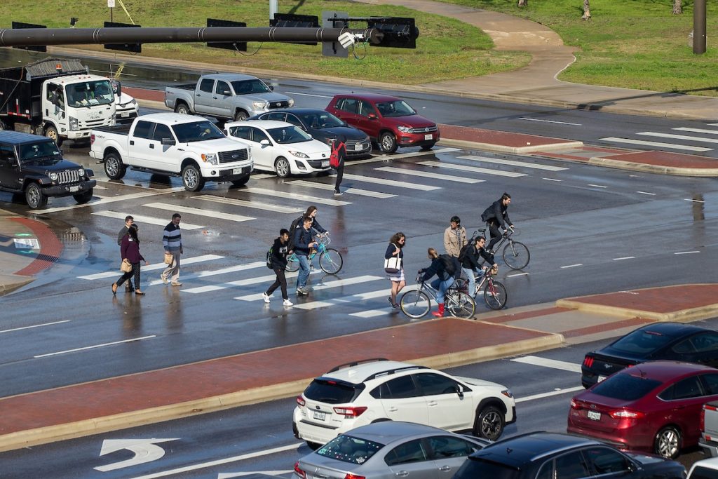 Cars, pedestrians and bicycle riders at busy intersection.