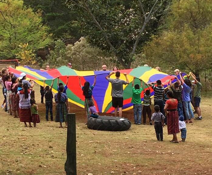 youth gathered around a brightly colored tarp work on a teamwork activity
