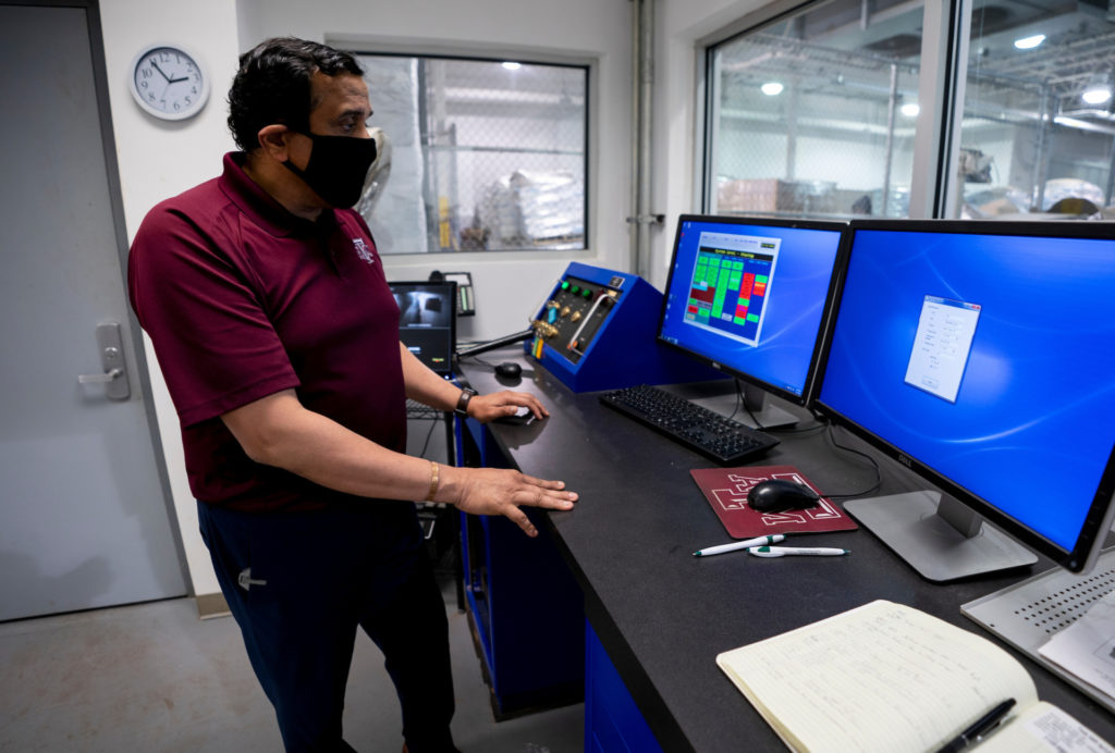 A man, Suresh Pillai, in a maroon shirt and mask stands in front of two blue computer screens of the eBeam control panel.