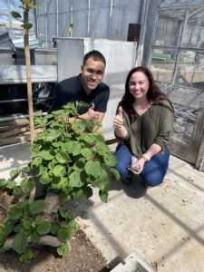 A young man, Christian Anguiano, and young woman, Kelsey Gipson, sit with a plant in a lab. 