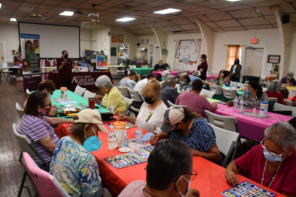 tables full of senior citizens with masks at St. Timothy's Senior Center in San Antonio playing nutrition bingo.