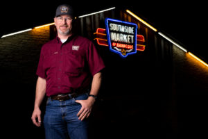 Bryan Bracewell '98 stands in front of Southside Market and Barbecue with the sign lit up behind him