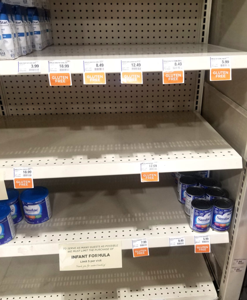 Store shelves with empty baby formula sections and a sign limiting purchased to 5 cans per person.