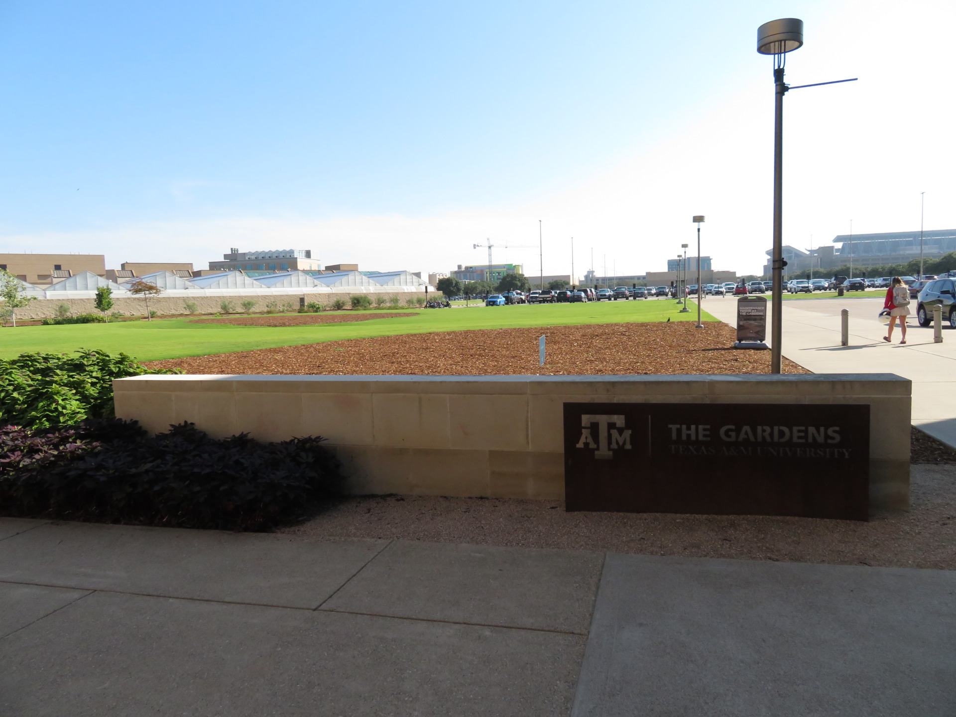 Empty planting bed next to low wall and The Gardens sign at the Leach Teaching Gardens at Texas A&M University. 