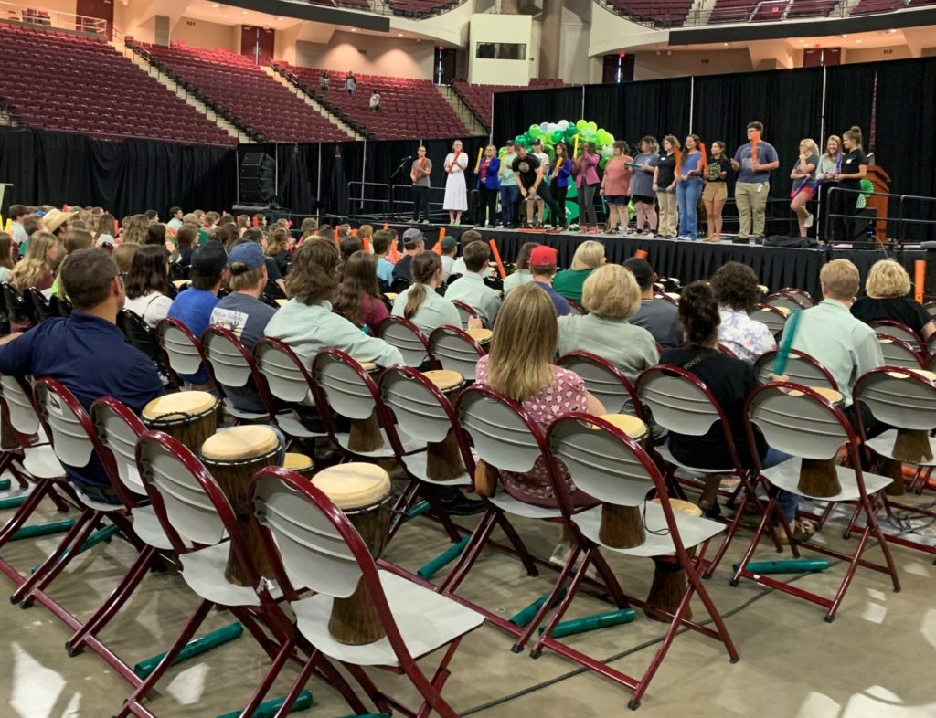 A large group of students stand on a stage in front of a large group of seated people during the LEAD academy at the 2022 Texas 4-H Roundup