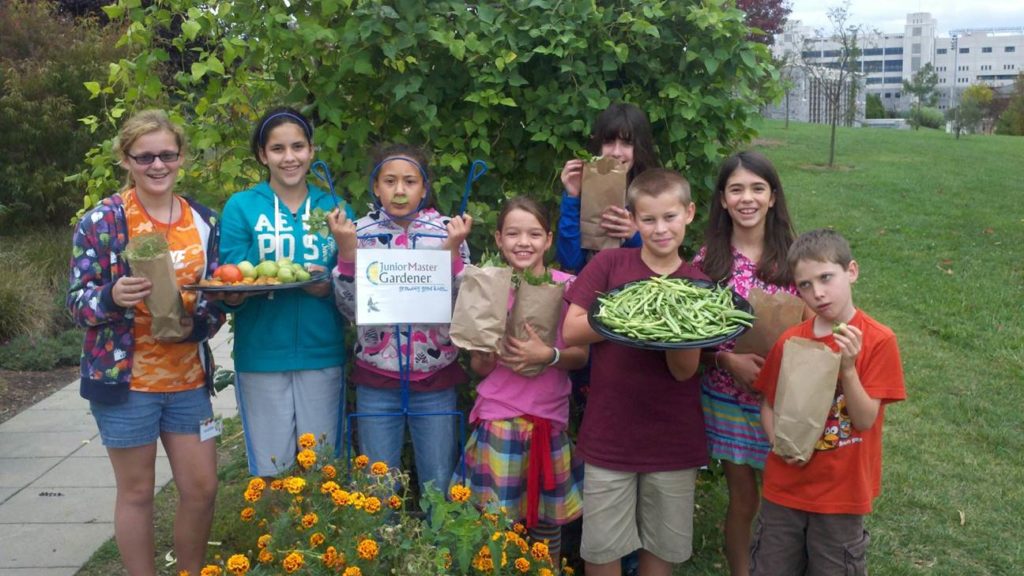 A group of kids holding up vegetables they've harvested as a part of the Junior Master Gardener 