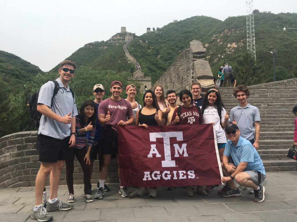 A group of students and advisors, including Won Bo Shim, pose with the Texas A&M Aggies flag in front of the Great Wall of China