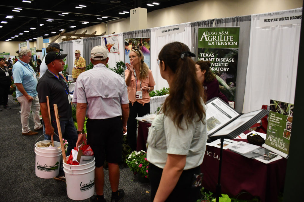 People stand on both sides of a table at a booth with a Texas A&M AgriLife banner in the background