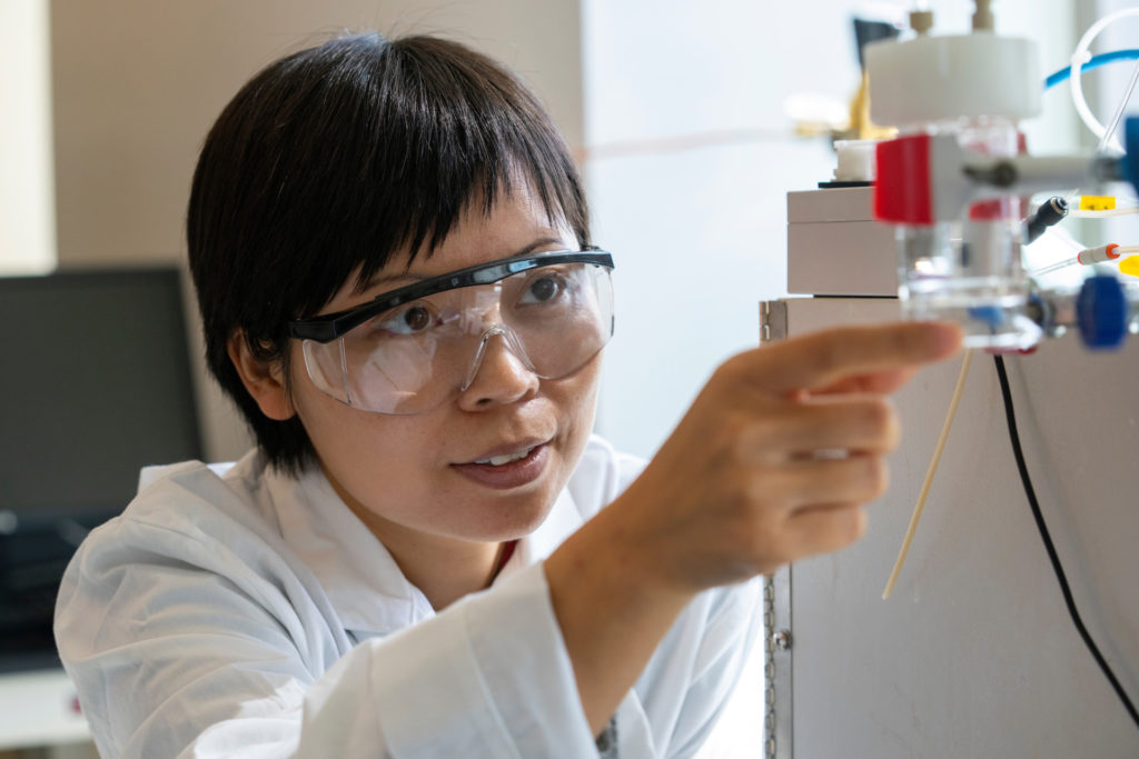 Susie Dai in camice e occhiali da lavoro al lavoro in un laboratorio sul sistema delle bioplastiche.