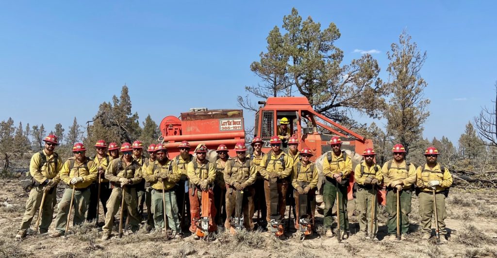 Lone Star State hand crew group photo in front of a large orange piece of equipment while assisting with California wildfires in 2021. 