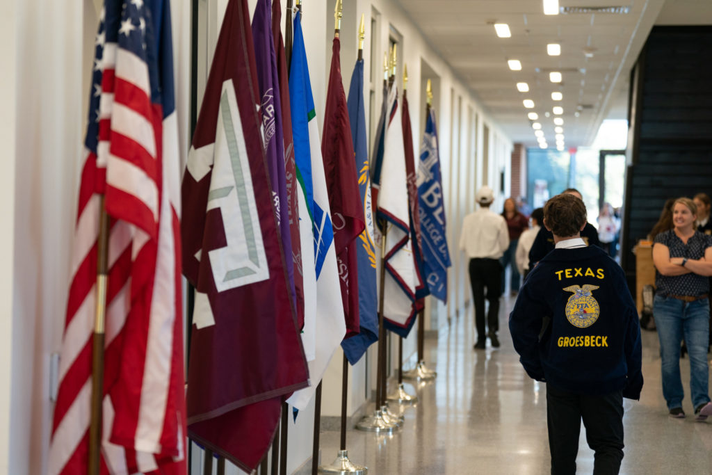 a row of flags line the left side of a hallway and a student walks away showing his FFA jacket