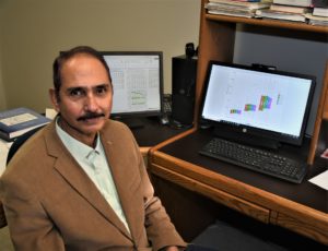 A man in a suit jacket, Prem Oli, sits in his office in front of a computer where he is modeling agricultural production systems