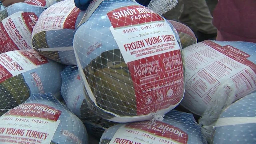 Many frozen labeled turkeys in a grocery store case.