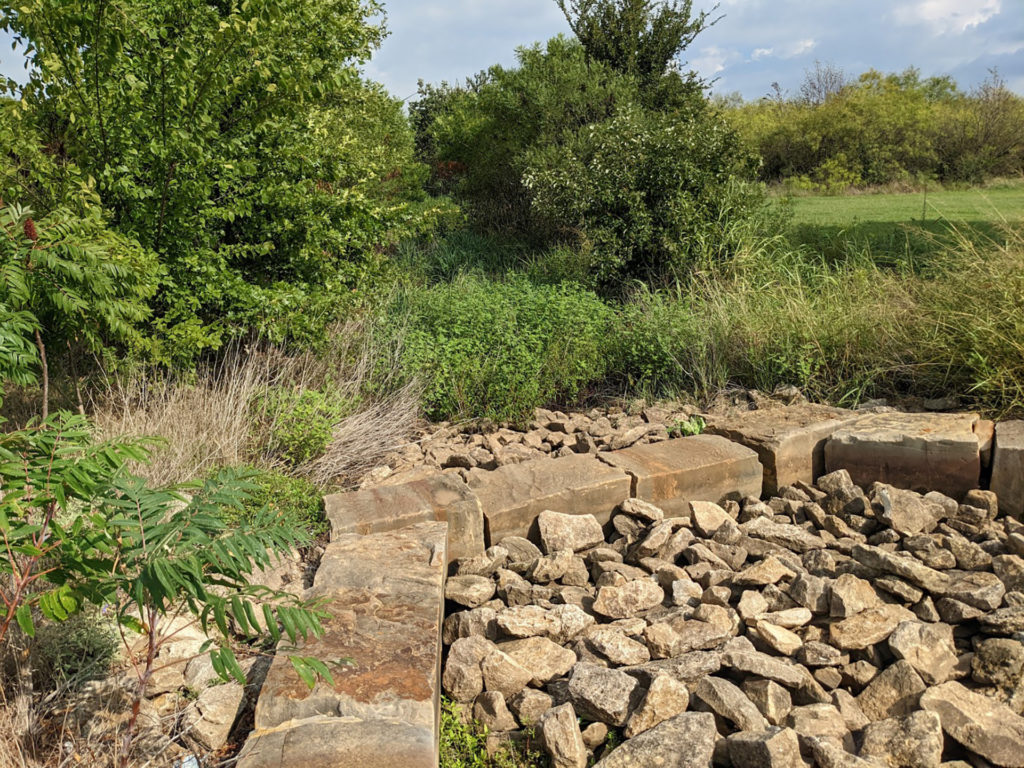 a stormwater retention area filled with rocks and surrounded by green vegetative growth 