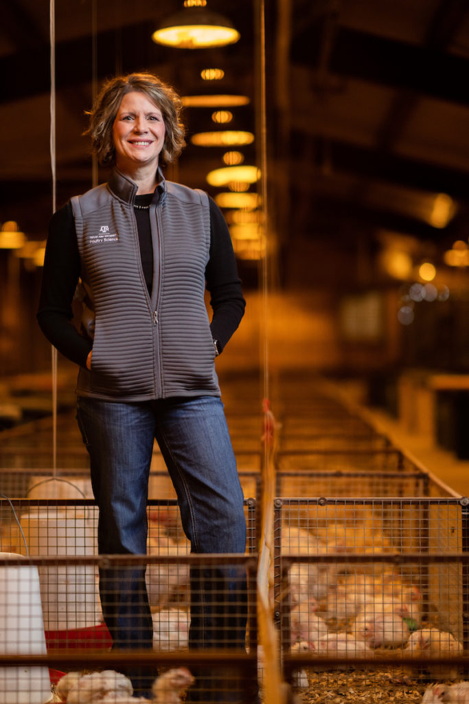 A woman, Dr. Audrey McElroy, stands among chicken cages in a large coop