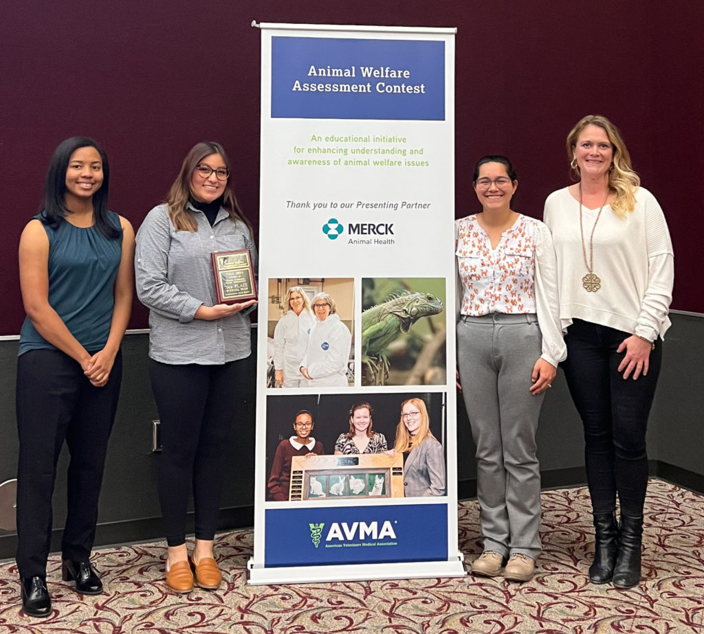 Four young women, two on each side of a large banner advertising the Animal Welfare Assessment Contest and sponsorship by Merck and AVMA, hold plaques to indicate their placing third.
