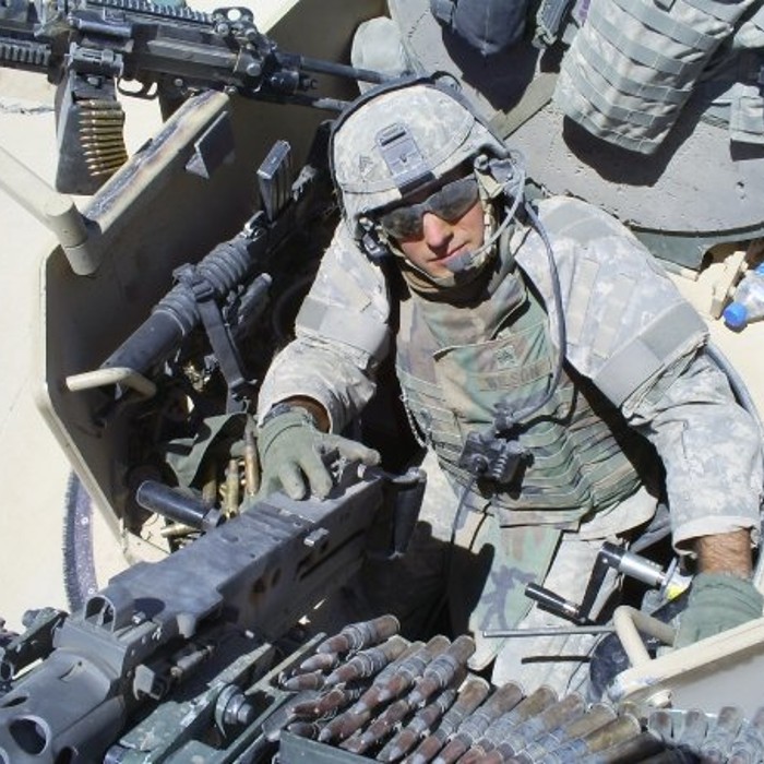 A man in full combat gear, Greg Wilson, sits in the gunners copula of an armored vehicle used to clear roads of improvised explosives 