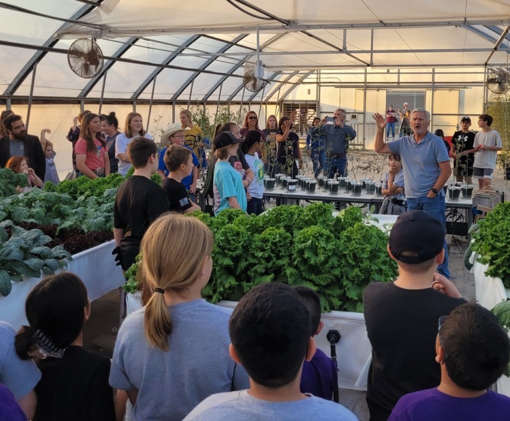 A man, Daniel Leskovar, explains hydroponic plant production to a group of STEM program students  
