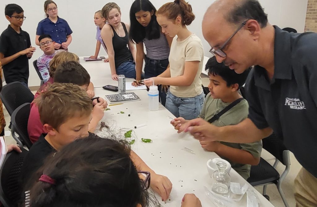 A man in glasses, Dr. Vijay Joshi, demonstrates an experiment on photosynthesis to STEM participants at the Texas A&M AgriLife Research and Extension Center in Uvalde