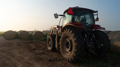 red tractor in front of hay bales with setting sun