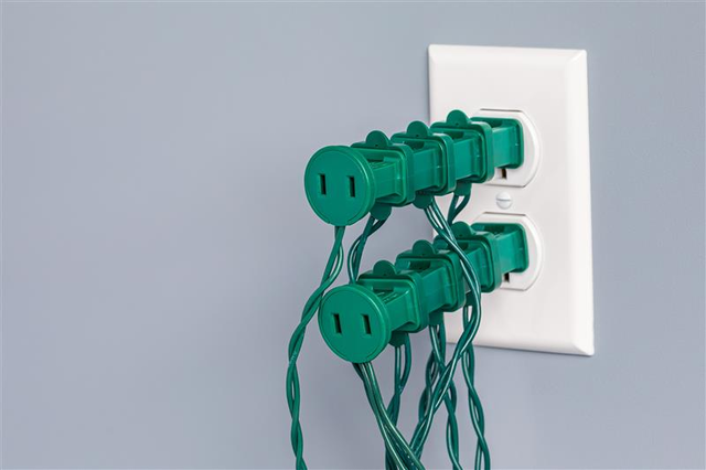 White electrical double outlet with four green back to back plugs piggie-backed on each outlet