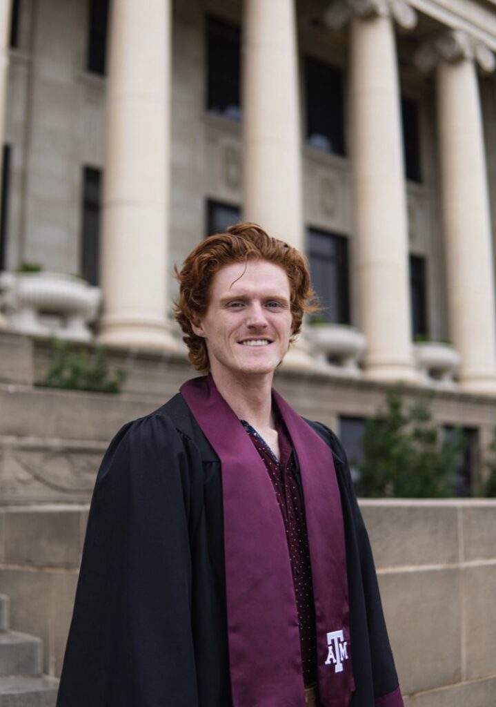 Campbell Webb stands in front of Texas A&M Administration building wearing graduate stole and robe