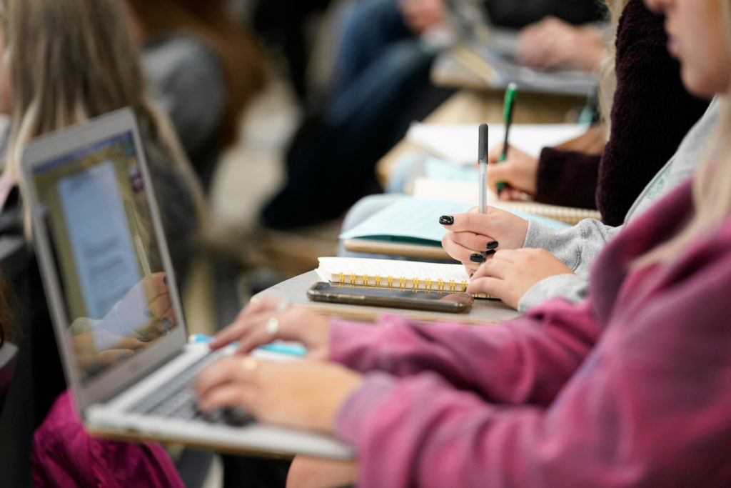 una fila de estudiantes trabajando en notas en una computadora y cuadernos