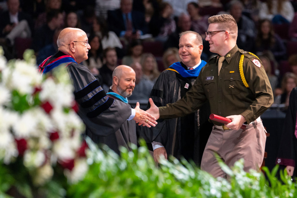 A man in military dress shakes hands on a College of Agriculture and Life Sciences graduation stage with others behind him