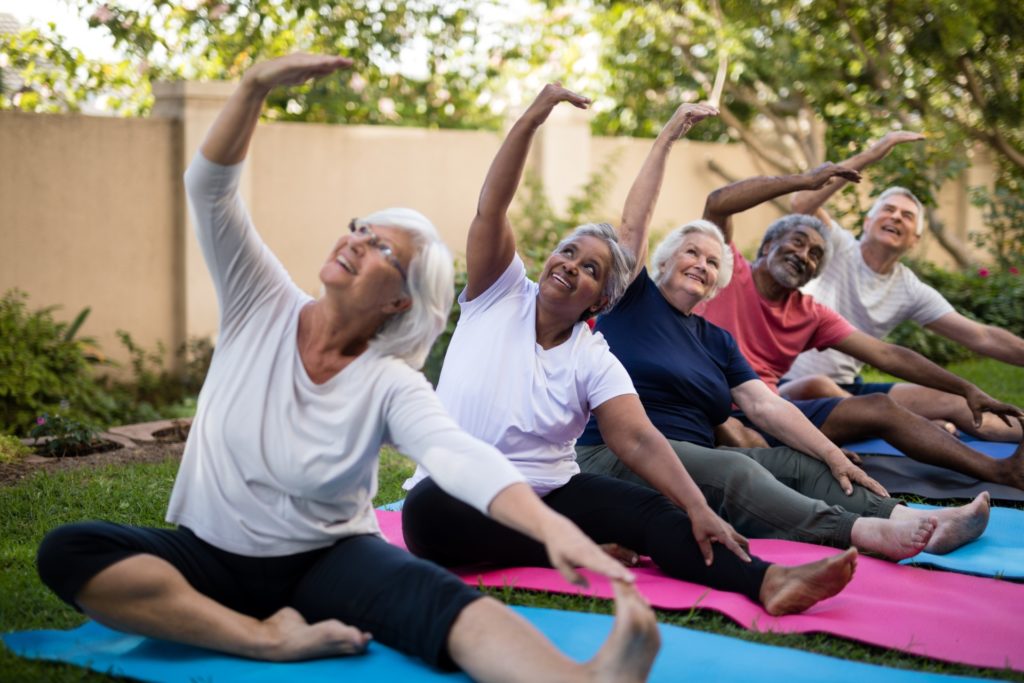 Aging adults with arms raised exercising at park