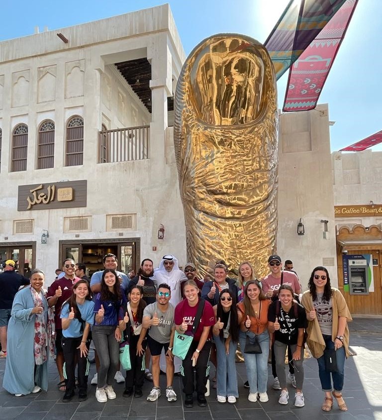 Texas A&M study abroad group in front of golden statue of giant thumb on street in Doha.