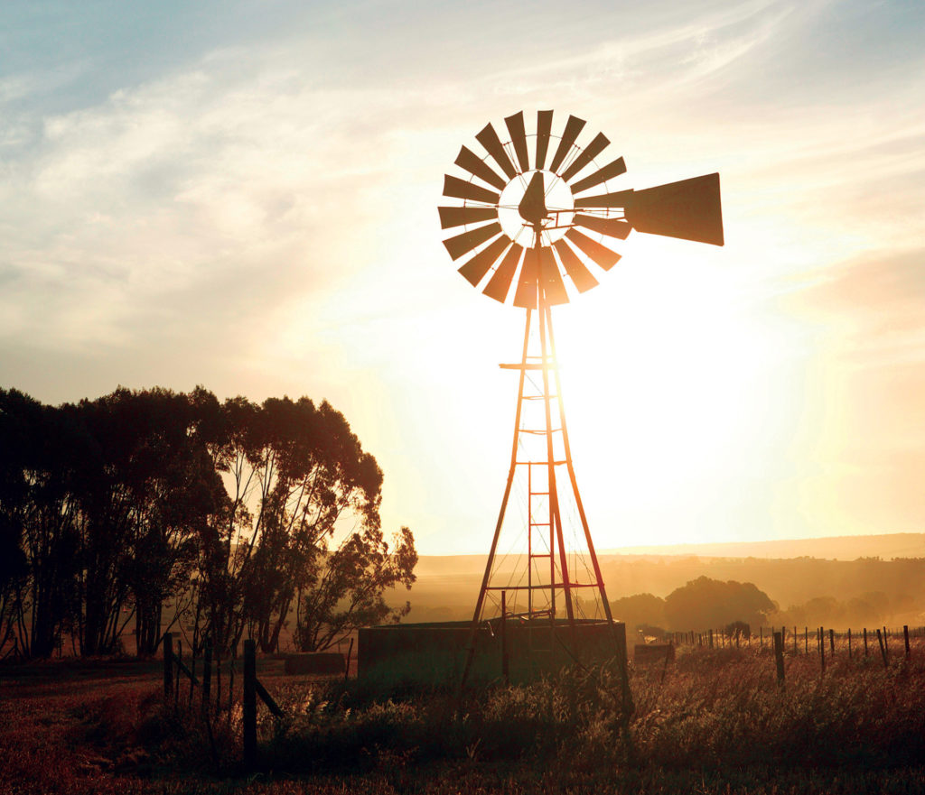 the sun sets on a windmill and stock tank filled by a water well
