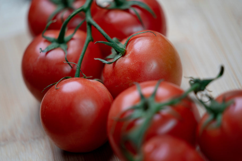 A cluster of bright red tomatoes on a stem sitting on a white table.