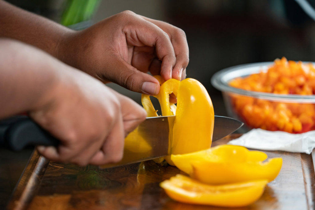 A pair of hands cuts a bright yellow pepper on a cutting board. Nutritious foods are important to Type 2 diabetes control.