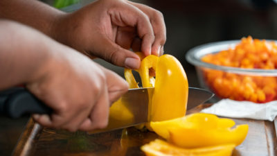 A pair of hands cuts a bright yellow pepper on a cutting board.