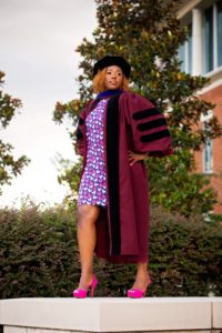 La ex alumna de ciencias avícolas, Alicia Walker, Ph.D., posa para una foto de graduación con su toga y birrete y un vestido con estampado de pollo.