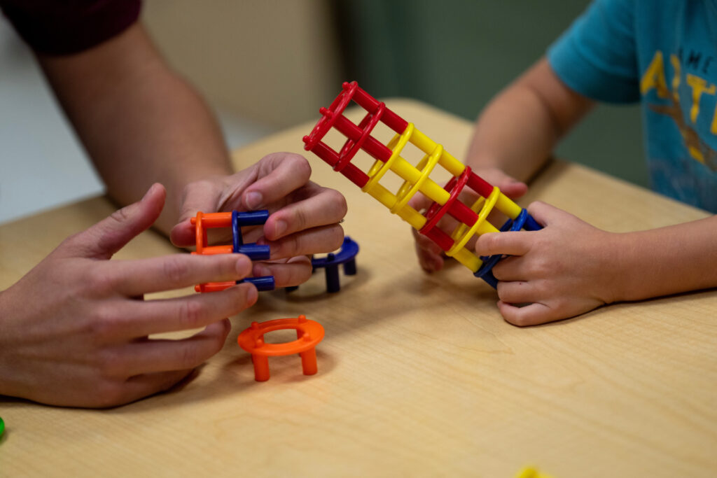 A pair of adult hands and a child hand's building colorful plastic towers of circular blocks. A OneOp webinar for professionals working with military students is March 29.