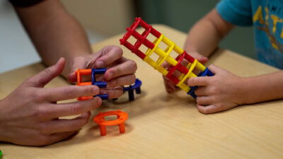 A pair of adult hands and a child hand's building colorful plastic towers of circular blocks.