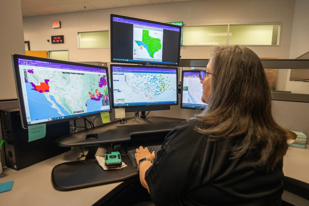 Belinda Jackson at computer station with multiple computer screens showing wildfire maps.