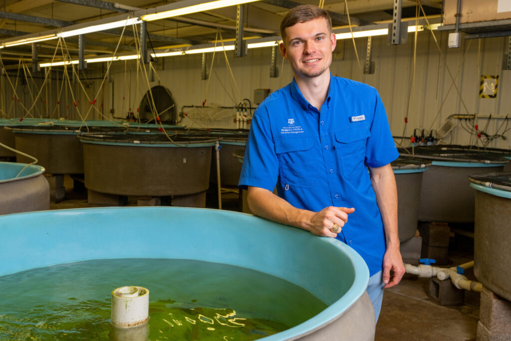 a young man in a blue shirt, Garrett Stamport, stands beside a tank of fish