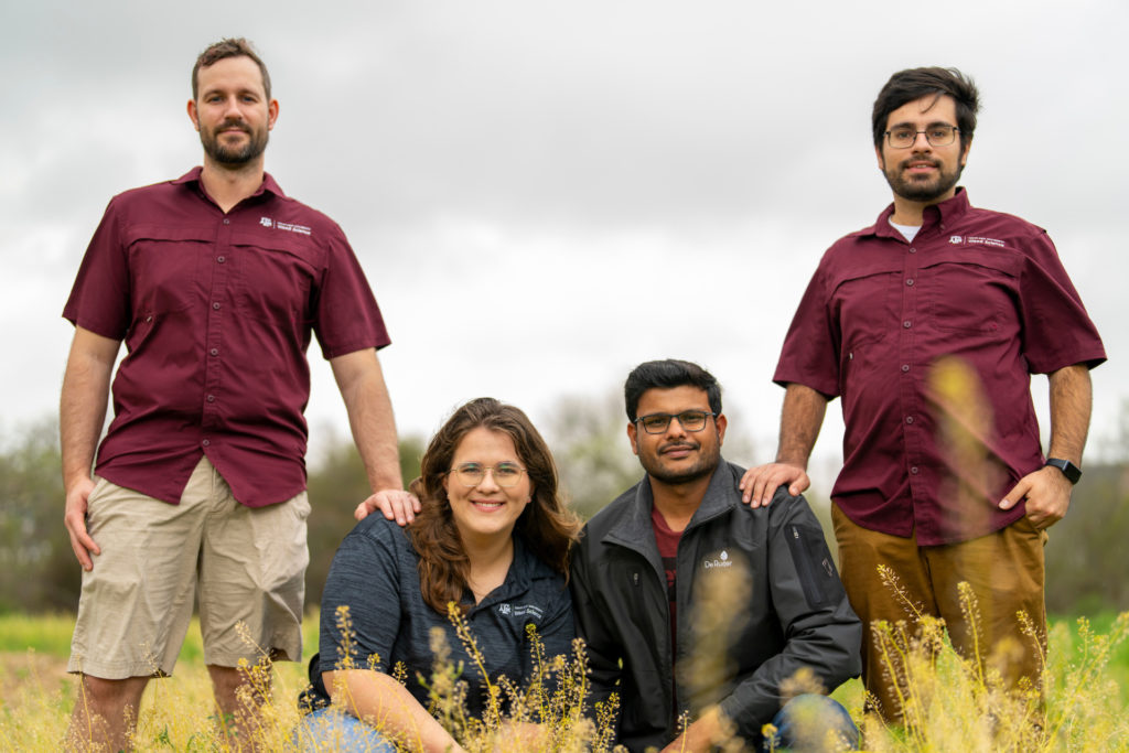 Weed science graduate students pose together in a field of weeds.