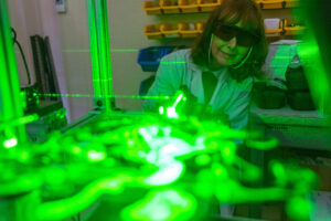 A green laser illuminates aerosolized particles with Dr. Maria King watching in the background.