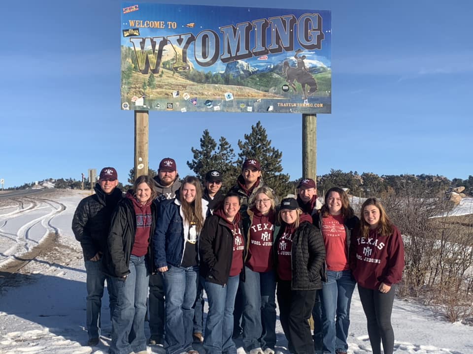 Los miembros del equipo de jueces de lana de Texas A&M posan frente a un letrero que dice: "Bienvenido a Wyoming."